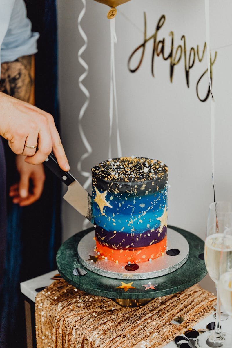 A colorful galaxy-themed cake being cut at a festive birthday party indoors.